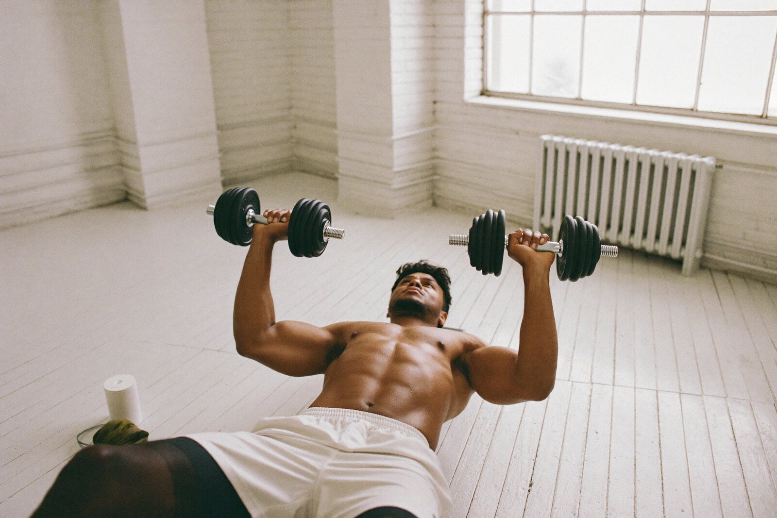 A lifter pressing dumbbells in a bright gym
